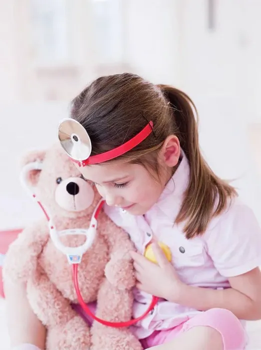 Framed Print : A young girl in a light pink shirt and toy medic attire playing with her teddy bear Framed Print : A young girl in a light pink shirt and toy medic attire playing with her teddy bear