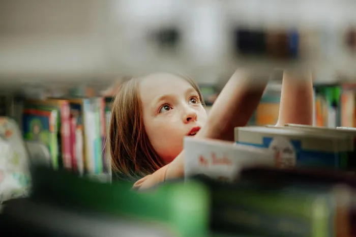 Framed Print : Young girl reaching for library book on shelf Framed Print : Young girl reaching for library book on shelf
