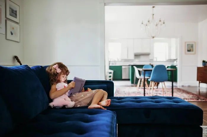 Framed Print : Young girl sitting on couch in modern living room learning on tablet Framed Print : Young girl sitting on couch in modern living room learning on tablet