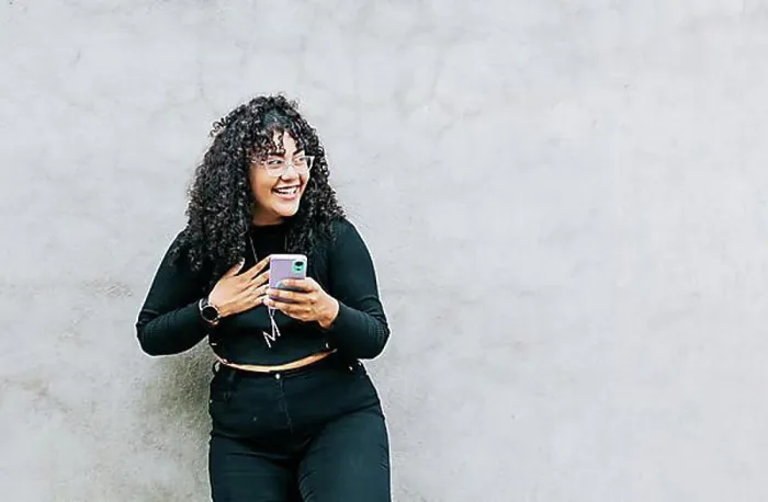 Framed Print : Young latin woman happy with her cell phone leaning against a wall Framed Print : Young latin woman happy with her cell phone leaning against a wall
