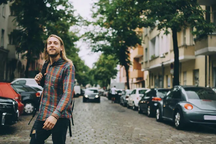 Framed Print : Young man carrying backpack while walking on cobbled street amidst cars in city