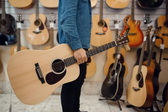Framed Print : Young man holding acoustic guitar in music store. Assortment in musical instruments shop, male musician buying equipment