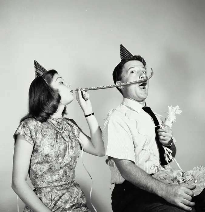 Framed Print : Young woman blowing a noisemaker near a young man's face