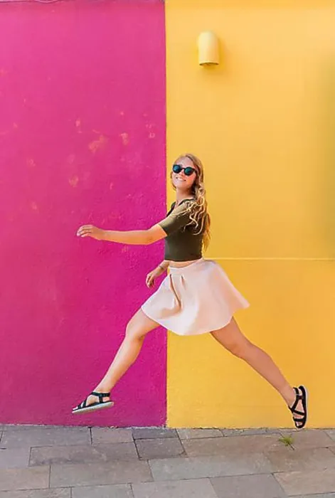 Framed Print : Young woman in dress jumps happily in front of colorful house Framed Print : Young woman in dress jumps happily in front of colorful house