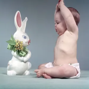 1950s BABY FULL FIGURE SEATED ARMS ABOVE HEAD LOOKING AT EASTER RABBIT TOY GREEN BOW FLOWERS 1950s BABY FULL FIGURE SEATED ARMS ABOVE HEAD LOOKING AT EASTER RABBIT TOY GREEN BOW FLOWERS