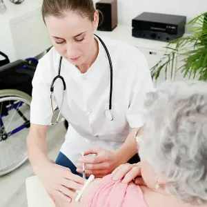 Cheerful young woman doctor giving vaccine injection to elderly woman at home Cheerful young woman doctor giving vaccine injection to elderly woman at home