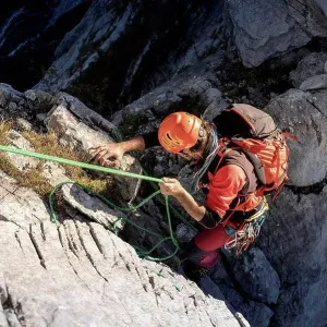 Determinant male Hiker moving down from mountain with rope on sunny day