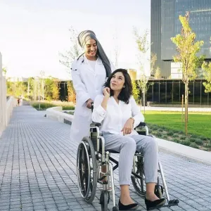 Disabled woman talking with female doctor pushing wheelchair on footpath Disabled woman talking with female doctor pushing wheelchair on footpath