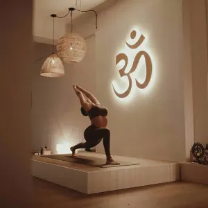 Female yoga instructor with arms raised bending while practicing by Om symbol Female yoga instructor with arms raised bending while practicing by Om symbol