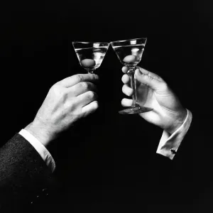 Two hands toasting with martini against black background Two hands toasting with martini against black background