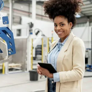 Happy businesswoman holding tablet PC standing in factory Happy businesswoman holding tablet PC standing in factory