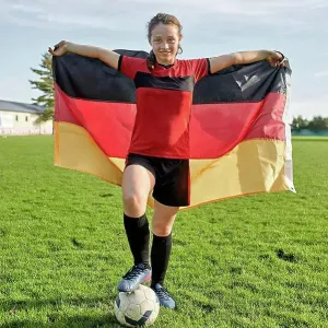 Happy girl standing with soccer ball and holding German flag on field Happy girl standing with soccer ball and holding German flag on field