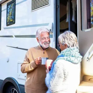 Happy senior couple holding coffee cup talking with woman by motor home