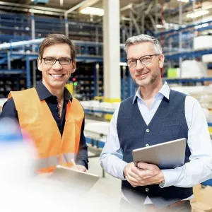 Happy worker standing by manager holding tablet PC in warehouse Happy worker standing by manager holding tablet PC in warehouse