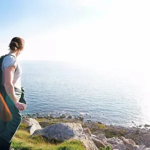Hiker with backpack on cliff looking at view of ocean, Portland, UK Hiker with backpack on cliff looking at view of ocean, Portland, UK