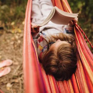 Little girl reads a book in hammock on a warm fall day while camping