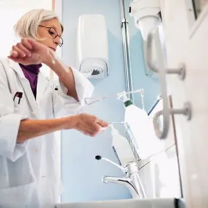 Low angle view of senior female doctor using soap dispenser to wash hands in bathroom Low angle view of senior female doctor using soap dispenser to wash hands in bathroom
