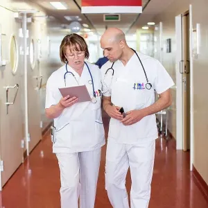 Male and female doctors using digital tablet while walking in hospital corridor Male and female doctors using digital tablet while walking in hospital corridor