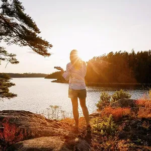 Rear view of woman holding mobile phone while standing on lakeshore at sunset Rear view of woman holding mobile phone while standing on lakeshore at sunset