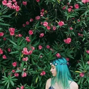 Serene young woman with blue hair standing below flowering tree