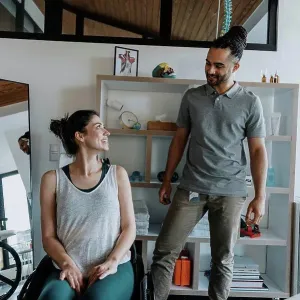 Smiling physiotherapist with female patient sitting on wheelchair in medical practice Smiling physiotherapist with female patient sitting on wheelchair in medical practice