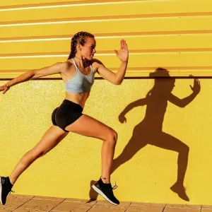 Young female athlete running by yellow wall Young female athlete running by yellow wall