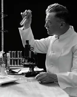 Manly Prints: 1920S 1930S 1940S Scientist Lab Technician In White Coat Looking At Test-Tube In Front Of Microscope
