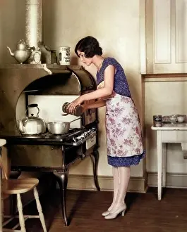 Story Prints: 1920s HOUSEWIFE AT GAS STOVE AND OVEN COOKING IN KITCHEN