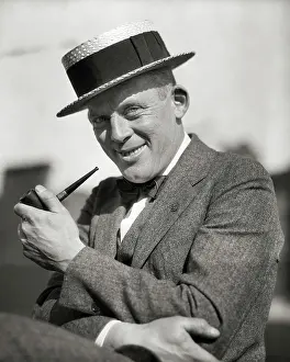 Expressions Prints: 1920s PORTRAIT SMILING MAN SMOKING A PIPE WEARING A STRAW BOATER STYLE HAT SUIT BOW TIE LOOKING AT CAMERA