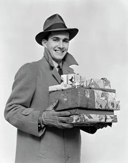 Gloves Prints: 1930S 1940S Man In Winter Coat Hat And Gloves Holding Pile Of Wrapped Christmas Presents Smiling