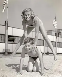 Frog Prints: 1930s 1940s SMILING GIRL AND BOY PLAYING LEAP FROG ON SAND BEACH BROTHER KNEELING BLONDE SISTER JUMPING OVER HIS BACK
