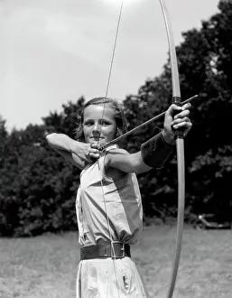 1930S Girl Wearing A Camp Jumper With Wide Leather Belt About To Release An Arrow From Bow