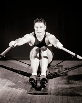 Focused Prints: 1930s MAN MUSCULAR ATHLETE CONCENTRATED FOCUSED FACIAL EXPRESSION EXERCISING WORKING OUT ON GYMNASIUM STATIONARY ROWING