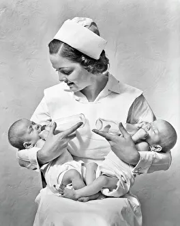 Astonished Prints: 1930s SMILING NURSE SITTING HOLDING JUGGLING TWO NEWBORN TWIN BABY GIRL SISTERS IN HER ARMS FEEDING THEM WITH BOTTLES