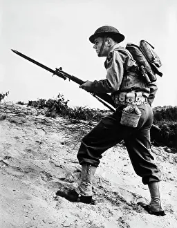 Boots Prints: 1940S 1942 World War Ii Soldier Walking Across Rough Terrain With Rifle And Bayonet In Hand