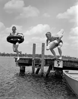 Physical Fitness Prints: 1940S 1950S Two Boys Wearing Inflatable Inner Tubes About To Jump In Lake Off Pier