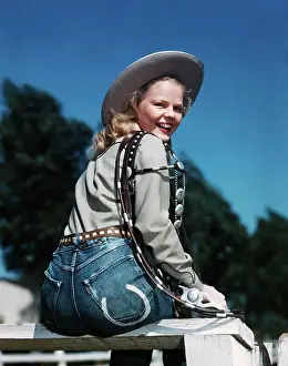 1940S 1950S Smiling Blond Woman Wearing Western Cowgirl Clothes Looking Over Shoulder Sitting On Wooden Fence