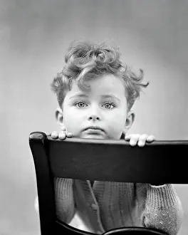 Expressions Prints: 1940s DIFFIDENT CURLY HAIR BOY RESTING CHIN ON BACK OF CHAIR LOOKING AT CAMERA