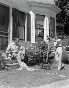 Sons Prints: 1940S Father Sits On Porch Steps Holding Rake Talking To Son Standing Holding Lawnmower Backyard Window Doorway