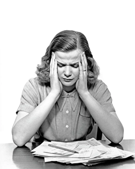 Depressed Prints: 1940s PANIC STRICKEN OVERWHELMED WOMAN HOLDING HER HEAD LOOKING DOWN AT PILE OF UNPAID BILLS ON THE TABLE