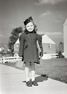 Lunch Prints: 1940s SMILING LITTLE GIRL READY FOR SCHOOL STANDING ON SIDEWALK WEARING BLACK HAT DOUBLE BREASTED COAT HOLDING LUNCH