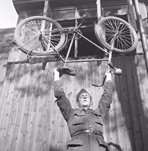 Soldiers Prints: 1940s soldier. A young man in uniform is balancing his bicycle above his head