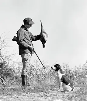 Mid Adultman Prints: 1940s YOUNG MAN HUNTER WITH SHOTGUN AND HUNTING DOG HOLDING BIRD PHEASANT