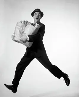 Runner Prints: 1950s 1960s HAPPY EXCITED MAN WEARING BUSINESS SUIT HAT CARRYING GROCERY SHOPPING BAGS RUNNING JUMPING IN AIR LOOKING