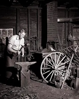 Blacksmith Prints: 1950s 1960s MAN LOCAL VILLAGE BLACKSMITH WORKING AS FARRIER SHAPING A HORSESHOE WITH HAMMER ON ANVIL IN FORGE VIRGINIA
