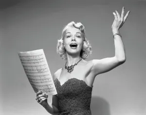 Singing Prints: 1950s BLOND WOMAN SINGING HOLDING SHEET MUSIC WEARING STRAPLESS DRESS NECKLACE Photographer: H