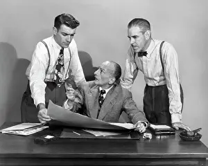 Innovation Prints: 1950s THREE BUSINESS MEN IN OFFICE STRATEGY CONFERENCE TWO STANDING ONE SEATED LOOKING AT PAPERS AND PLANS