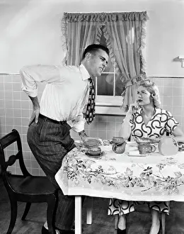 Mid Adultman Prints: 1950s COUPLE AT BREAKFAST TABLE MAN WITH HAND ON HIP SUFFERING BACK PAIN
