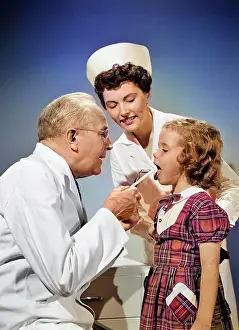Doctors Prints: 1950s MAN DOCTOR EXAMINING MOUTH OF LITTLE GIRL CHILD WITH WOOD TONGUE DEPRESSOR WHILE WOMAN NURSE IS LOOKING ON