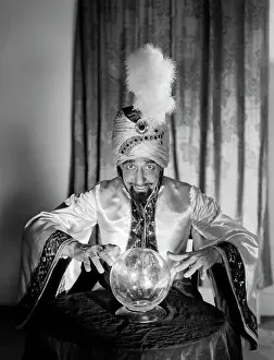 Advice Prints: 1950S Portrait Man Soothsayer Swami Fortune Teller Wearing Robe And Feather In Turban Gazing Over Crystal Ball